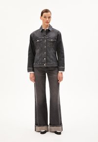 Zwarte spijkerjas met knoopsluiting, twee voorkwestjes en contrasterende manchetten. Gecombineerd met hoge zwarte flared jeans.