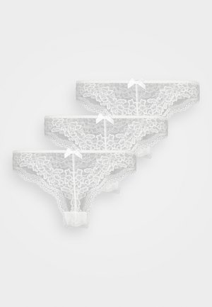 Set di pantaloni in pizzo bianco, con bordi ondulati e motivi floreali, decorati con piccoli fiocchi sul davanti. Tre pezzi esposti.