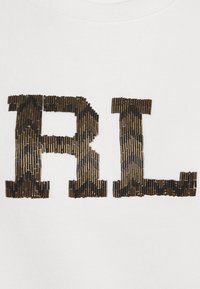 Bílá mikina s textem "R.L." vyrobeným z hnědých a černých vzorovaných korálků, která ukazuje vyvýšený design a různé tvary.