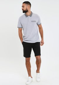 Grå polo-shirt med en kontrasterende krave og lomme-detalje, parret med sorte shorts og hvide sneakers. Glat tekstur, afslappet pasform.