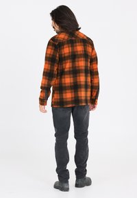 Orange og sort ternet flannel skjorte med en afslappet pasform, lange ærmer og knapmanchetter, båret over mørkegrå jeans og fodtøj.