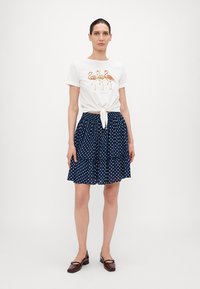T-shirt blanc avec un imprimé flamant rose et un devant noué, associé à une jupe navy à pois. La jupe présente un design en niveaux et une taille élastique.