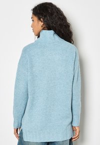 Jasnoniebieski, oversize sweter wykonany z miękkiego materiału dzianinowego. Wysoki kołnierz, długie rękawy oraz boczne rozcięcia u dołu dla zwiększenia komfortu.