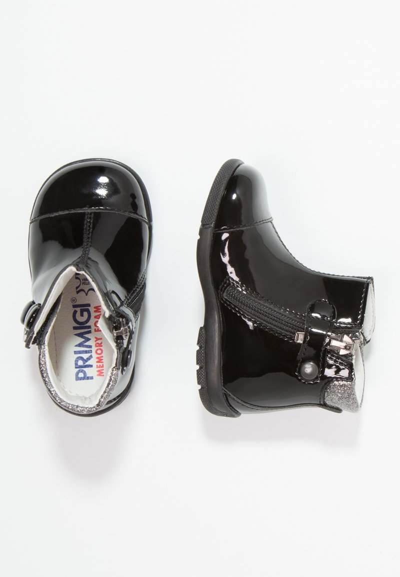 Bottes cheville en cuir verni noir avec accents argentés, fermeture éclair latérale et semelle en caoutchouc texturée. Intérieur doté de mousse à mémoire de forme.