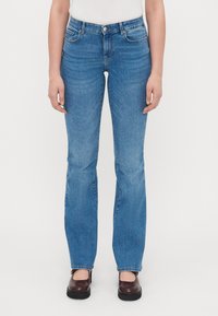 Siniset suorat farkut, joissa on viisi taskua, haalistunut pinta, messinkinen napin suljenta ja lievä venyvyys, yhdistetty tummanruskeisiin luistimiin.