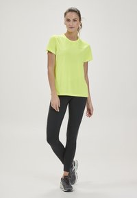 Neon gul sport t-shirt med korta ärmar och rund halsringning, i kombination med svarta, åtsittande leggings med en sidologotyp.