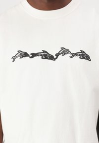 Weißes Baumwoll-T-Shirt mit einem schwarzen abstrakten Delphin-Druck auf der Brust. Klassisches Rundhalsdesign mit kurzen Ärmeln.