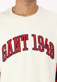 Biała bluza z czerwonymi i granatowymi akcentami. Posiada duży haftowany napis "GANT 1949" na piersi. Ribbed okrągły dekolt, miękka tekstura.