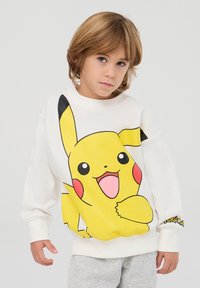 Felpa bianca con una grande grafica colorata di Pikachu, con dettagli neri sulle maniche e un logo "Pokémon" ricamato sul polsino.