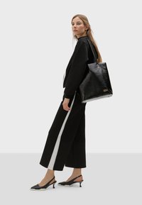 Crna kožna torba s teksturiranim finišem, trokutastog oblika, s zlatnim hardverom i detaljem logotipa na dnu.