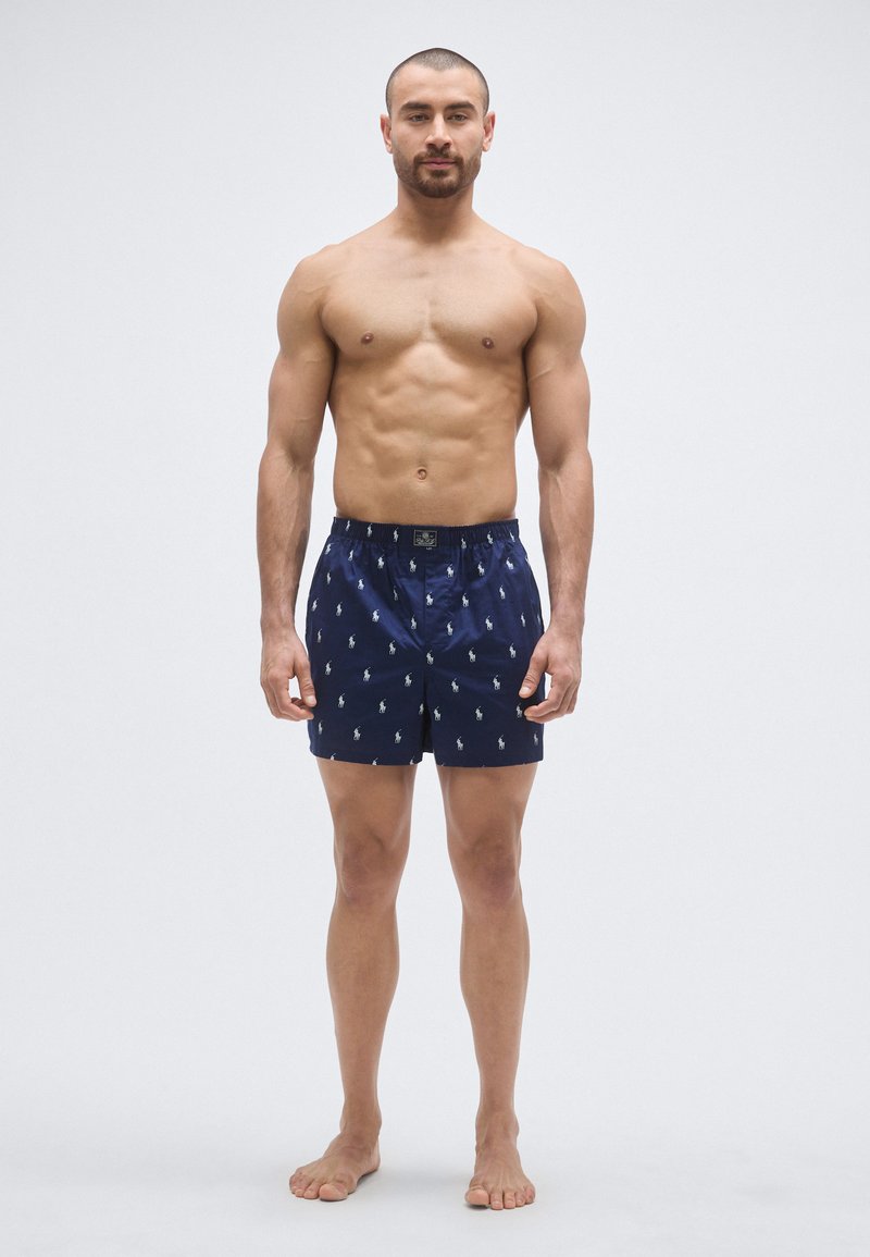 Tmavomodré plavecké šortky z ľahkej tkaniny, s opakujúcim sa vzorom malého loga koňa, elastickým pásom a bočnými vreckami.