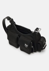 Bolsa transversal preta em nylon com três bolsos exteriores com fechos de correr e um detalhe em fivela prateada sobre um fundo branco.