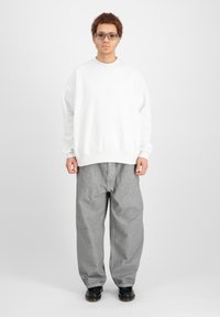 Bijela oversized dukserica s rebrastim manžetama, uparena s širokim sivim trapericama. Outfit je upotpunjen crnom obućom.