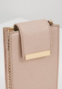 Różowo-złota torebka z ekoskóry o teksturowanej powierzchni, z prostokątną klapką i złotym akcentem metalowym. Posiada pasek na łańcuszku.