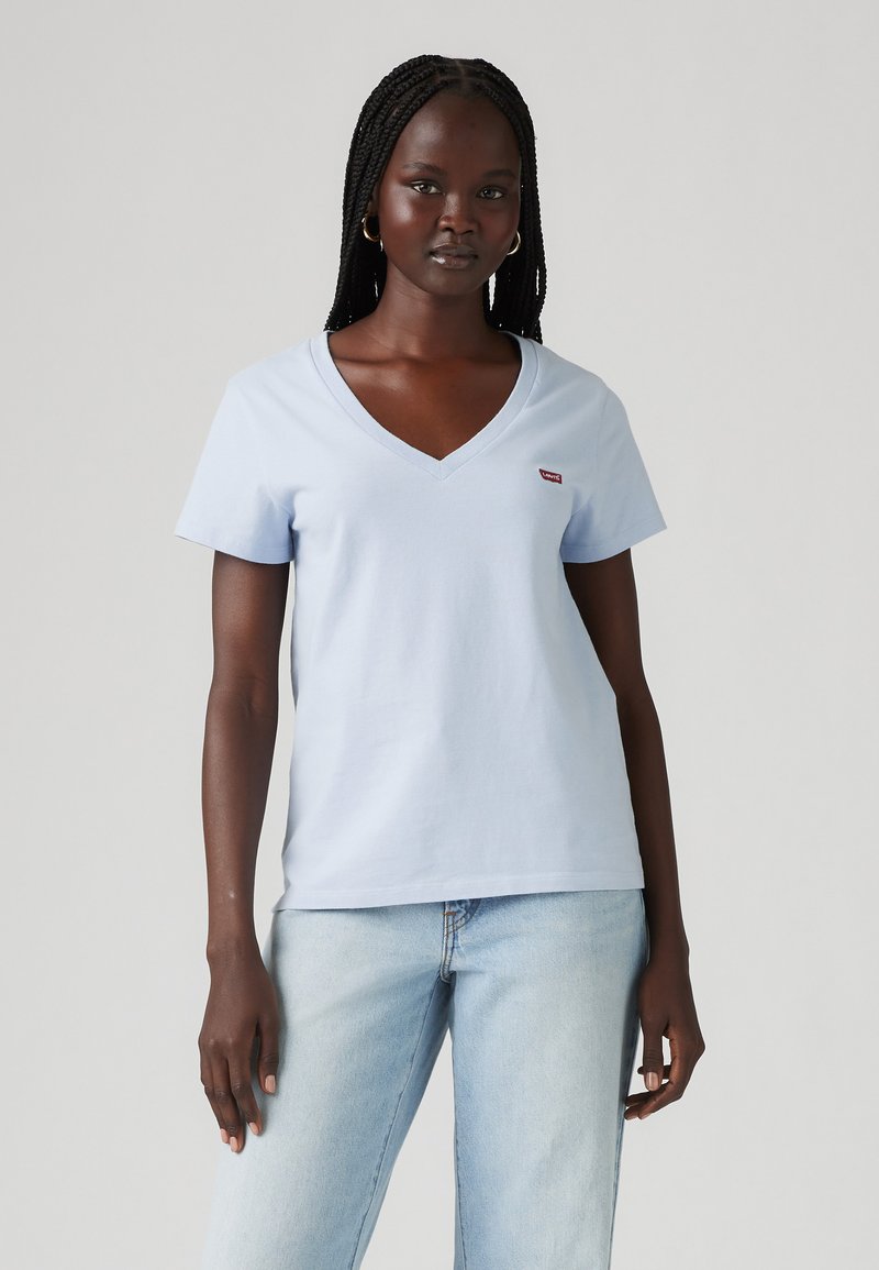 Camiseta de cuello en V azul claro hecha de algodón suave. Presenta mangas cortas y un pequeño logo rojo en el lado izquierdo del pecho. Corte clásico y diseño minimalista.