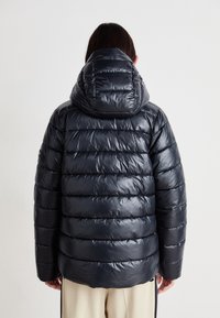Casaco puffer em azul marinho escuro, com um acabamento brilhante, painéis acolchoados horizontais e um capuz grande. Projetado para proporcionar calor e conforto.
