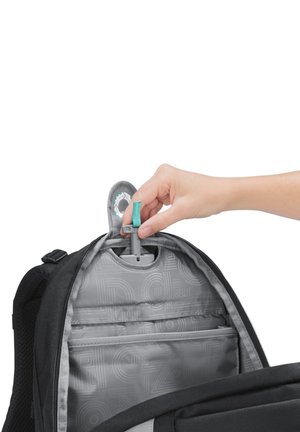 Main tire une sangle turquoise attachée au porte-clés du compartiment intérieur à l'intérieur d'un sac à dos noir et gris ouvert.