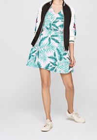 Vestido floral en rosa claro con patrón de hojas verdes, cintura entallada y falda acampanada. Chaqueta bomber negra con acentos florales. Zapatillas blancas.