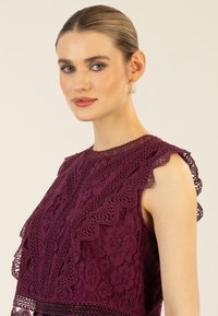 Spitzenoberteil in einem tiefen Burgunderrot mit gewellten Kanten und floralen Mustern. Akzentuiert durch zarte Details und eine strukturierte Oberfläche.