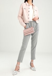 Jasnoróżowa kurtka z korduroju w kroju cropped, biała bluzka, szare dopasowane spodnie z bocznymi paskami, różowa torebka crossbody oraz metaliczne srebrne szpilki.