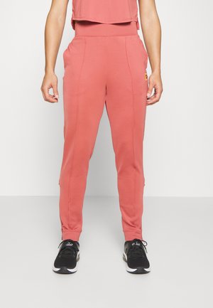 Calças de jogging rosas com pernas afuniladas, cintura elástica, detalhes de costura e bolsos laterais. Combinadas com ténis de atletismo pretos.