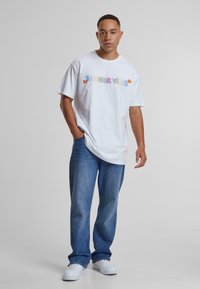 Camiseta de algodón blanca con el texto colorido "SUMMER VIBES" en el pecho, combinada con jeans de mezclilla azul claro y zapatillas blancas.