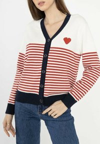 Gilet rayé rouge et blanc avec des accents navy, présentant un col en V, cinq boutons et un petit détail en forme de cœur rouge sur la poitrine gauche.