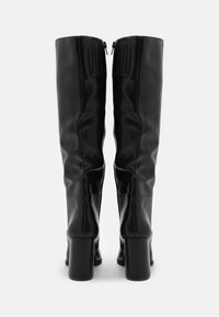 Bottes noires montantes jusqu'aux genoux en cuir lisse, dotées d'un talon bloc et d'une fermeture éclair arrière avec un accent texturé en haut.