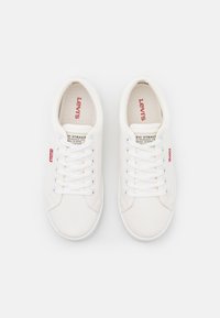 Witte canvas sneakers met een gestructureerd oppervlak, een ronde neus en platte witte veters. Voorzien van rode logo-accenten en branding op de tong.