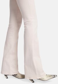 Flared lichtroze jeans gecombineerd met puntige hakken met een slangachtig textuur, in een zwart-wit kleurenschema en met een lage silhouet.