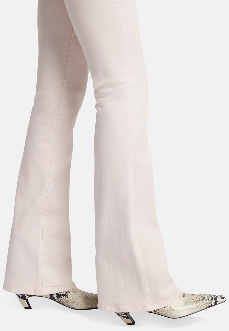 Jean flares rose clair associés à des talons aiguilles au motif serpent, présentant une palette de couleurs noir et blanc et une silhouette basse.