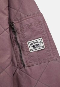Quilted jacket in mauve fabric featuring a side zipper and a rectangular label with text, "ORIGINALS GUESS AUTHENTIC STYLE."