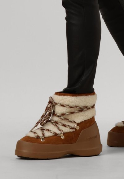 Bruine suède en crèmekleurige faux bont enkellaarzen met decoratieve veters, rubberen zolen en metallic oogjes. Zachte textuur, casual ontwerp.