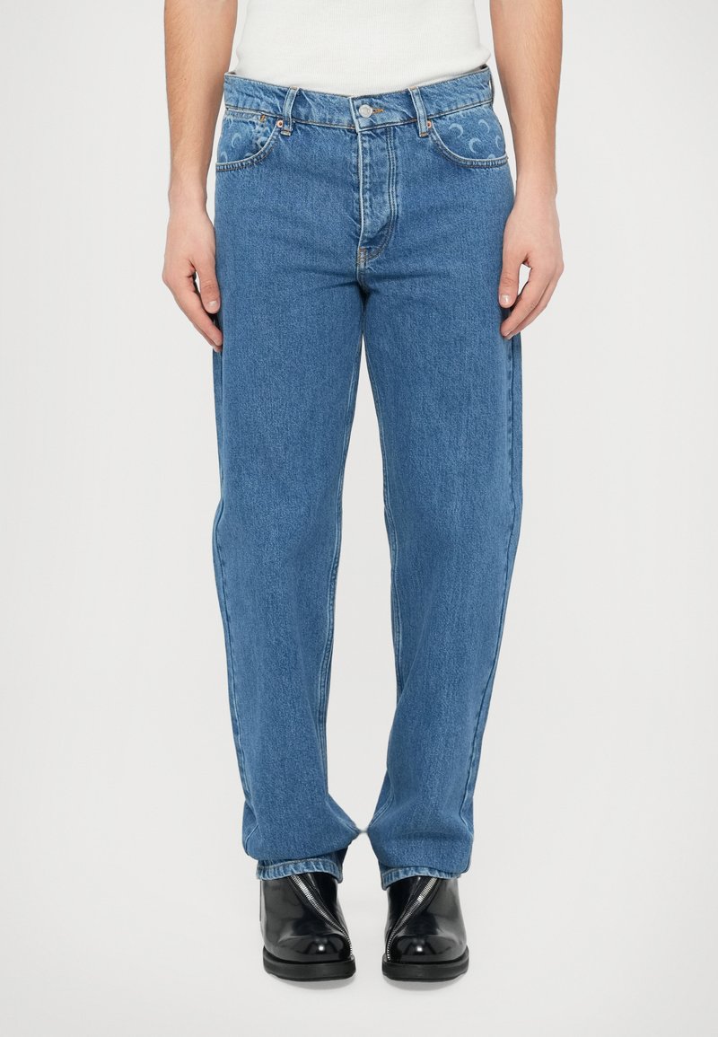 Svetlo modre denim hlače s pravim krojem, okrašene z vezenimi vzorci na žepih in kontrastnim šivom. Oblečene s črnimi čevlji.