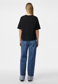 Melna īsām piedurknēm t-kreklā, kas valkāta ar augsto jostasvietu, brīvā griezuma, gaiši zilu džinsu, kuru malās ir sarullēti ādere un aizmugurējās kabatas.