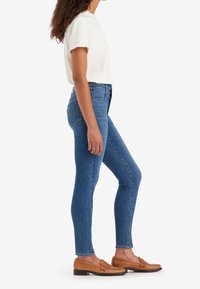 Camiseta de color gris claro, jeans ajustados de cintura alta en azul y mocasines en color marrón claro. Textura de denim suave, ajuste casual y silueta esbelta.