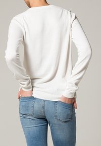 Witte gebreide trui met lange mouwen, ronde hals en geribbelde manchetten. Gecombineerd met lichtblauwe denim jeans met achterzakken.