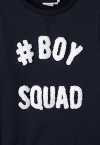 Felpa blu navy con lettere bianche in rilievo e soffici: "#BOY" sopra "SQUAD", caratterizzata da un colletto rotondo e polsini a costine.