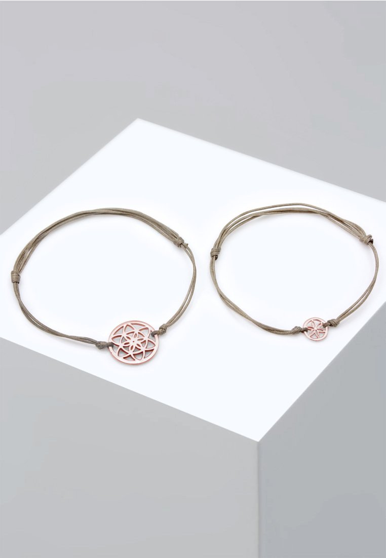 Två justerbara armband gjorda av beige snöre, med runda rosa geometriska berlockar. Det ena armbandet är större än det andra.