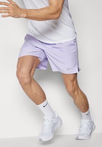 Licht lavendel sportshorts met een gladde textuur, voorzien van een klein grijs Nike-logo. Gdragen met witte Nike-sokken en sneakers.