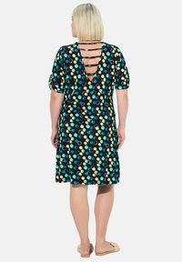 Kleid mit kurzen Ärmeln aus dehnbarem Stoff, mit schwarzem Grund und mehrfarbigen Punkten sowie einem tiefen V-Ausschnitt mit trägerdetail.