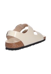 Sandal beige con due fasce larghe, soletta in sughero e suola in gomma nera. Presenta una superficie liscia e dettagli in metallo dorato.