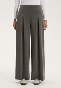 Szerokie, szare spodnie z plisami z przodu, usztywnioną talią i gładką teksturą. Połączone z jasnymi trampkami z akcentami.