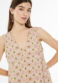 V-pääntie ilman hihoja oleva mekko, jossa on beige, vaaleanpunainen ja ruskea geometrinen kuvio. Pehmeää kangasta, joka on virtaava ja rento malli.