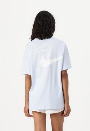 T-shirt oversized blu chiaro realizzato in cotone, con un grande logo Nike bianco e la scritta "Swoosh" sulla schiena. Maniche corte e vestibilità rilassata.