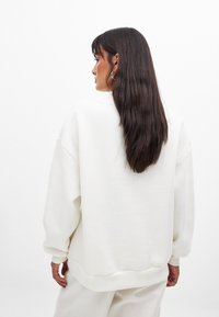 Biała, przepuszczająca bluza oversize z miękkiego materiału, z opadłymi ramionami i ściągaczami, prosty dół i luźny krój.