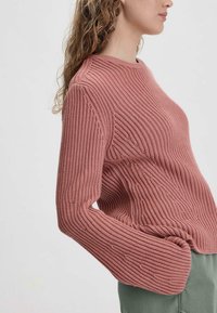 Rippstrickpullover in staubigem Rosa mit rundem Halsausschnitt und leicht übergroßen Ärmeln, kombiniert mit olivgrünen Hosen.