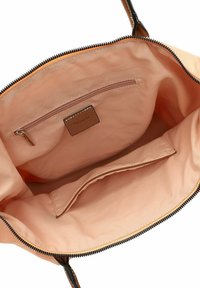 Interno della borsa in pelle color cuoio con una tasca con cerniera e una tasca aperta, caratterizzato da una fodera in tessuto pesca e dettagli neri della cerniera.