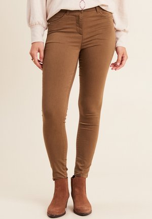 Jeans skinny marroni realizzati in un tessuto elasticizzato, con vita media, tasche frontali e una texture liscia. Abbinati a stivaletti alla caviglia.
