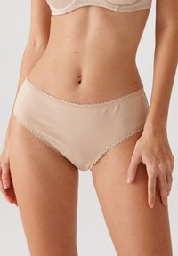 Beige katoenen slip met gekartelde kant langs de tailleband. Gladde textuur, lage taille en een eenvoudige, ingetogen vorm.